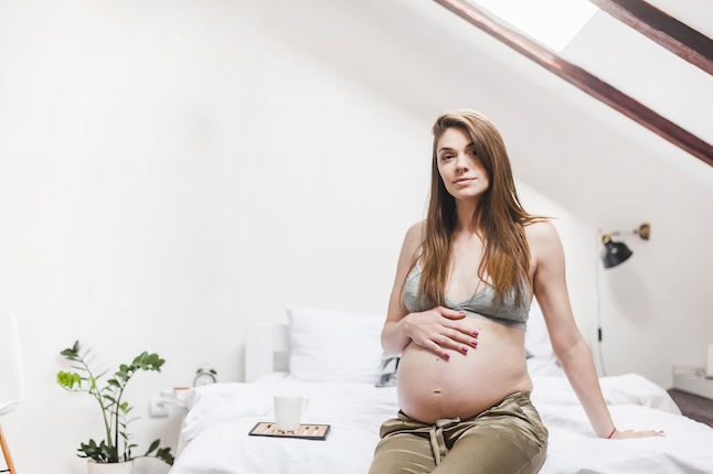 relaxed-pregnant-woman-with-coffee-mug-sitting-bed